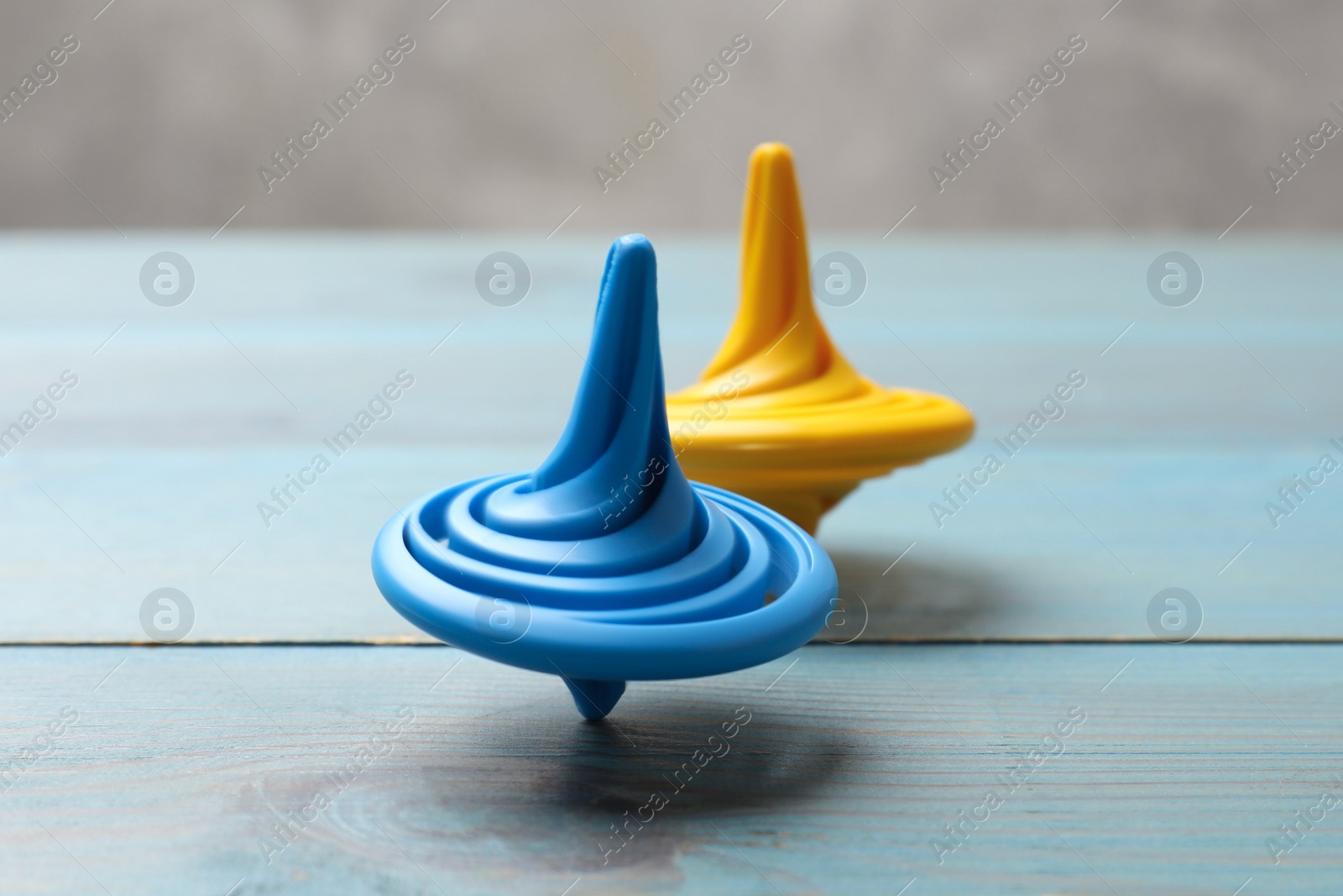 Photo of Bright spinning tops on light blue wooden table, closeup