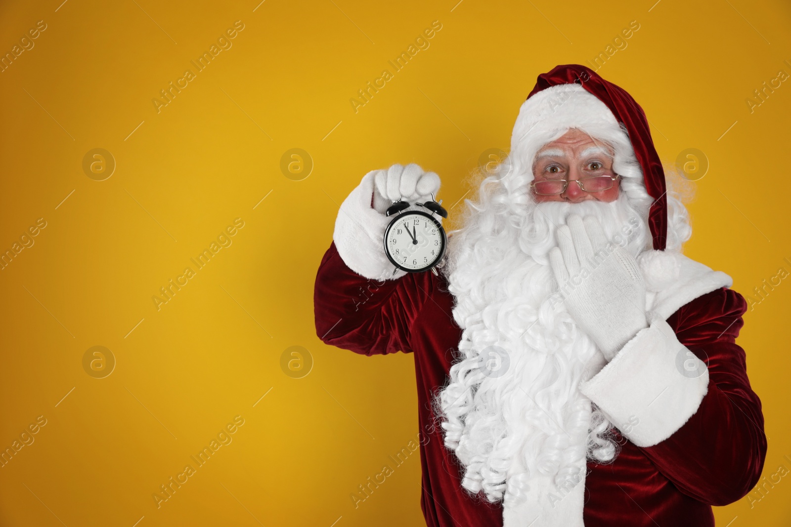 Photo of Santa Claus holding alarm clock on yellow background, space for text. Christmas countdown