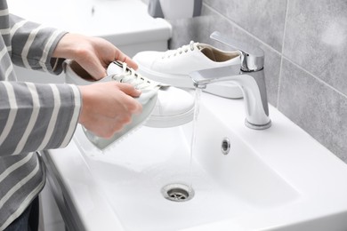 Woman washing stylish sneakers with brush in sink, closeup