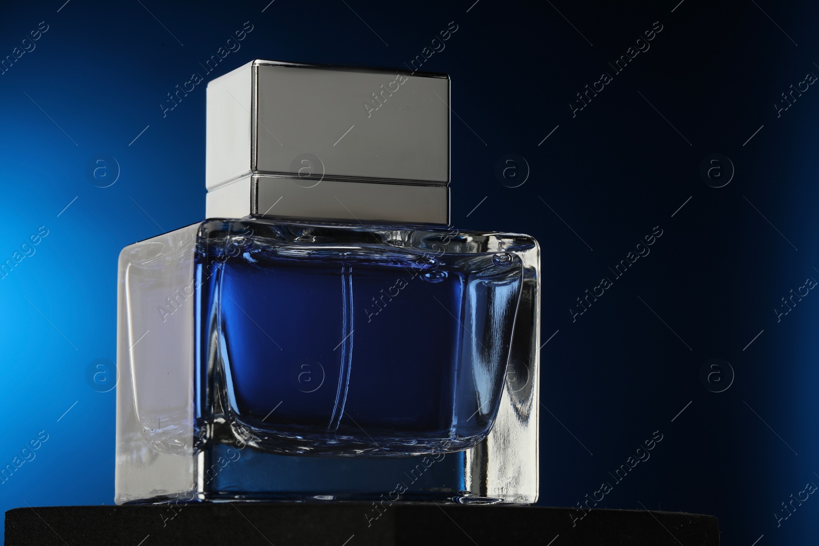 Photo of Luxury men`s perfume in bottle against dark blue background, closeup. Space for text