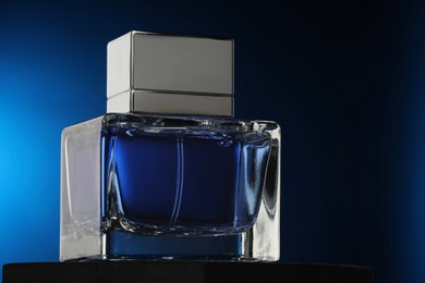 Photo of Luxury men`s perfume in bottle against dark blue background, closeup. Space for text