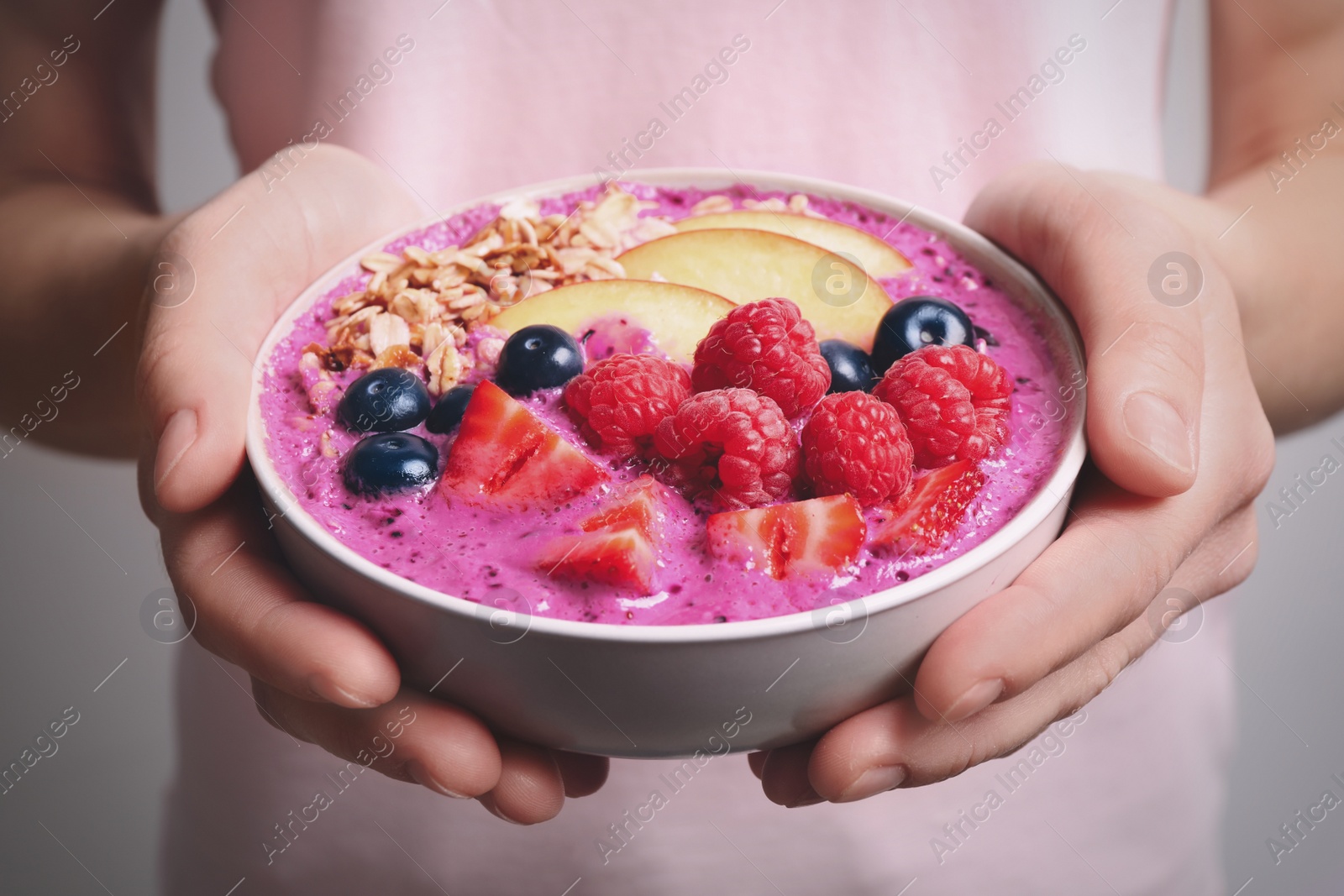 Photo of Woman holding bowl with tasty acai smoothie and fruits on light grey background, closeup