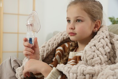 Photo of Little girl holding nebulizer for inhalation at home