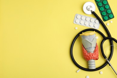 Photo of Plastic model of thyroid with tumor, pills and stethoscope on yellow background, flat lay. Space for text