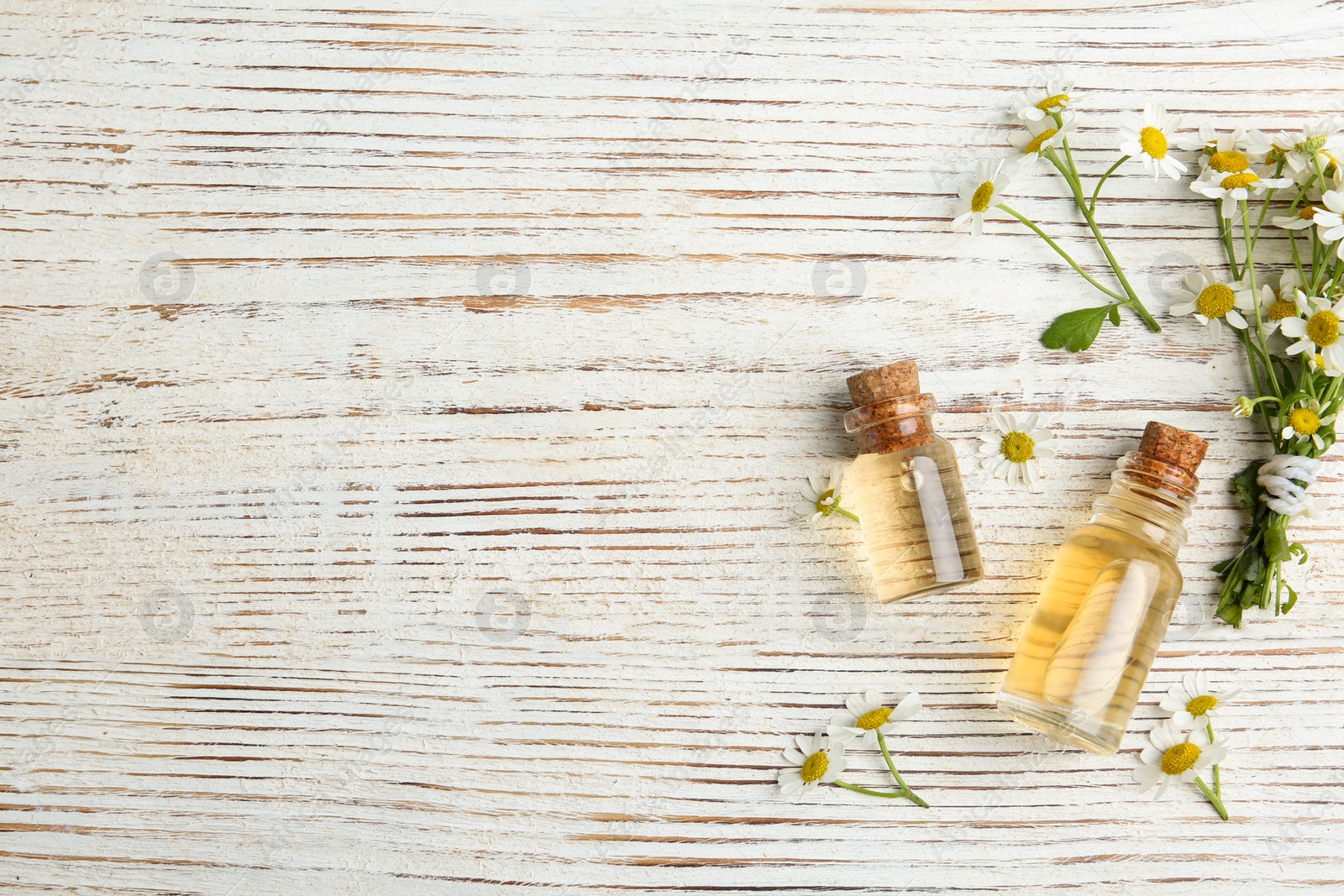 Photo of Bottles of essential oil and chamomiles on white wooden table, flat lay. Space for text