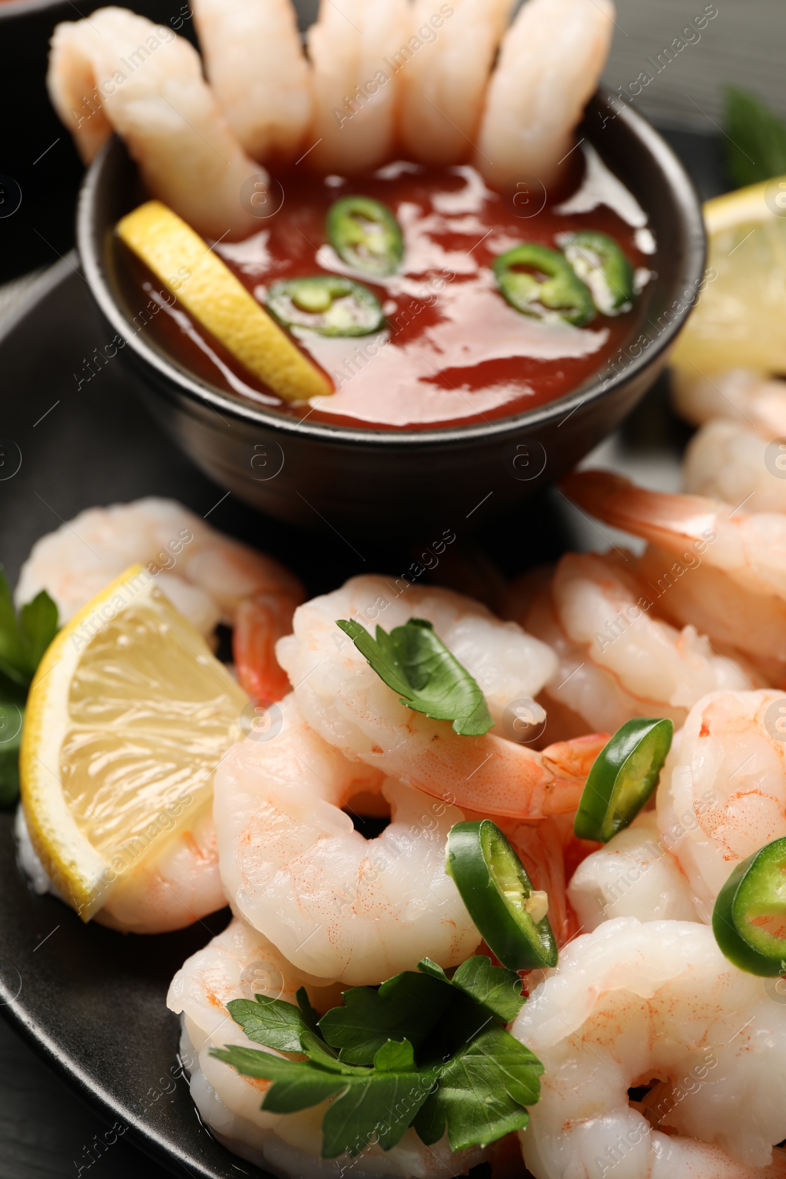 Photo of Tasty boiled shrimps with cocktail sauce, chili, parsley and lemon on table, closeup