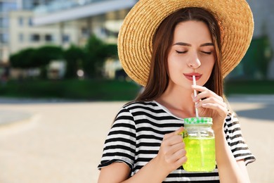 Photo of Young woman in straw hat with plastic cup of fresh juice outdoors, space for text