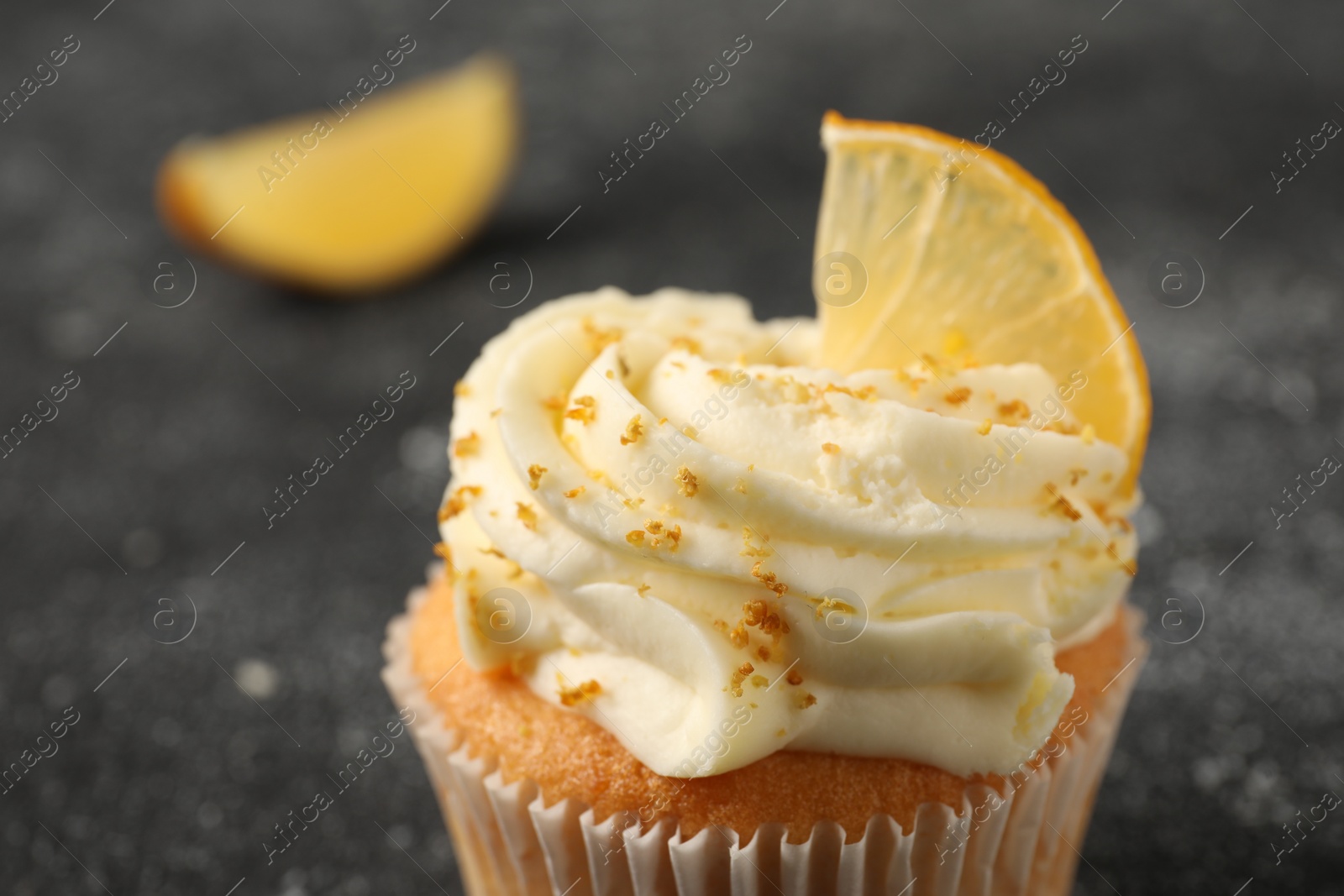 Photo of Tasty cupcake with cream, zest and lemon slice on black textured table, closeup