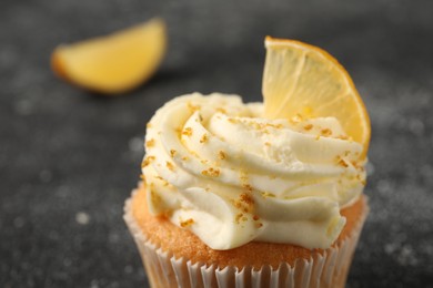Photo of Tasty cupcake with cream, zest and lemon slice on black textured table, closeup