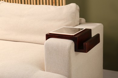 Tablet on sofa armrest wooden table in room. Interior element