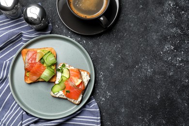 Tasty toasts with salmon, cream cheese and cucumber on black table, top view. Space for text