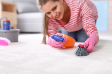 Photo of Young woman cleaning carpet at home