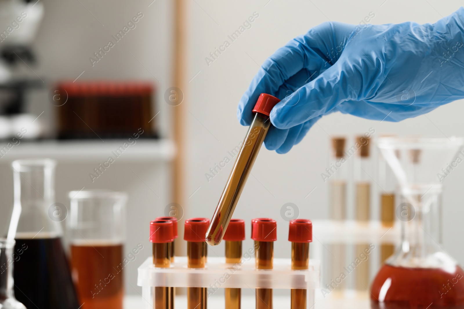 Photo of Scientist taking test tube with brown liquid from stand, closeup