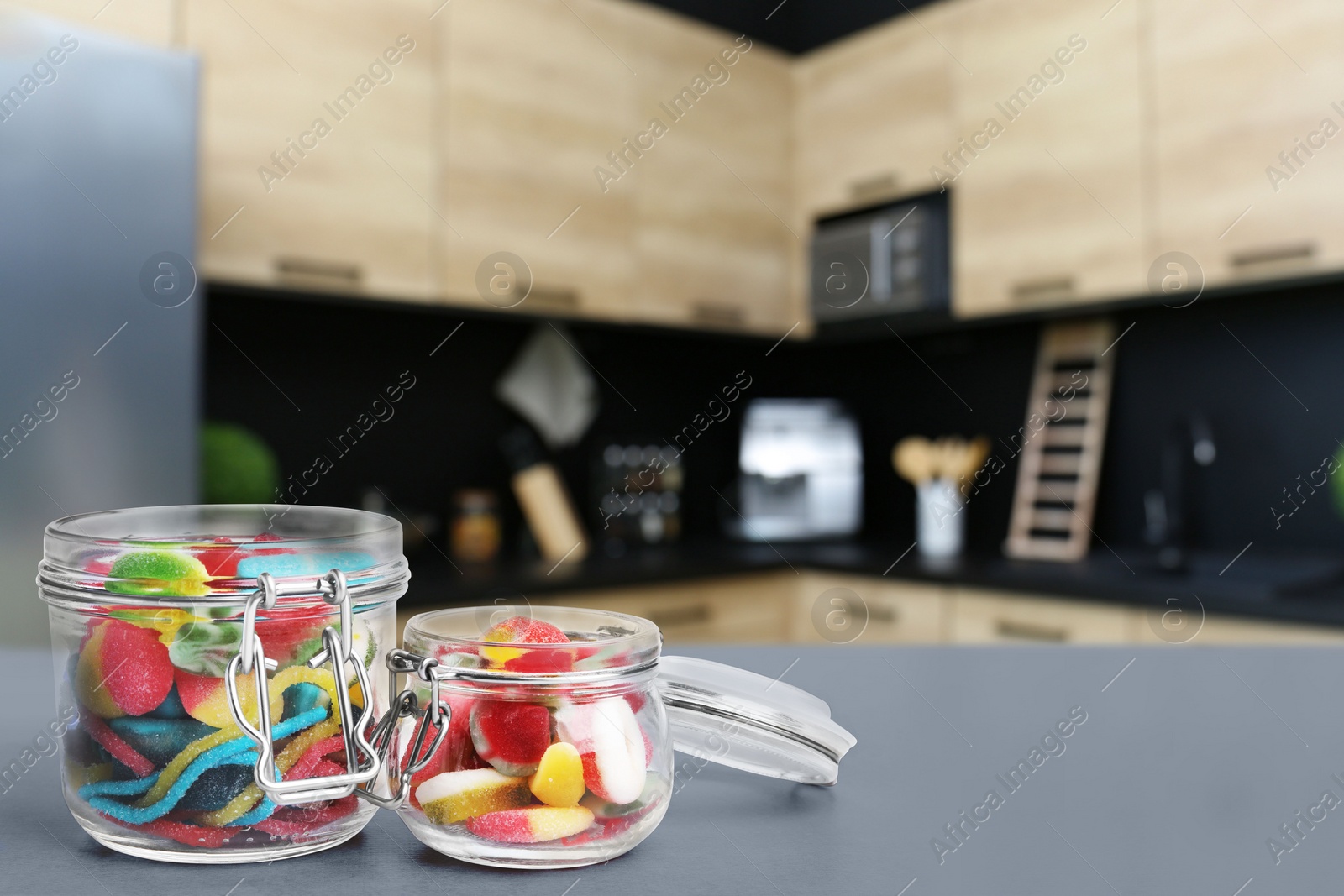 Image of Glass jars with tasty gummy candies on grey table in kitchen. Space for text