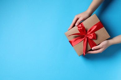 Photo of Woman with gift box on light blue background, top view. Space for text