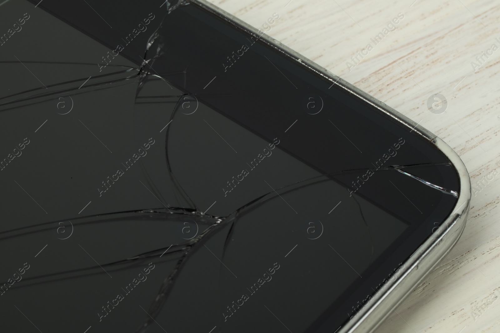 Photo of Smartphone with cracked screen on light beige wooden background, closeup. Device repair