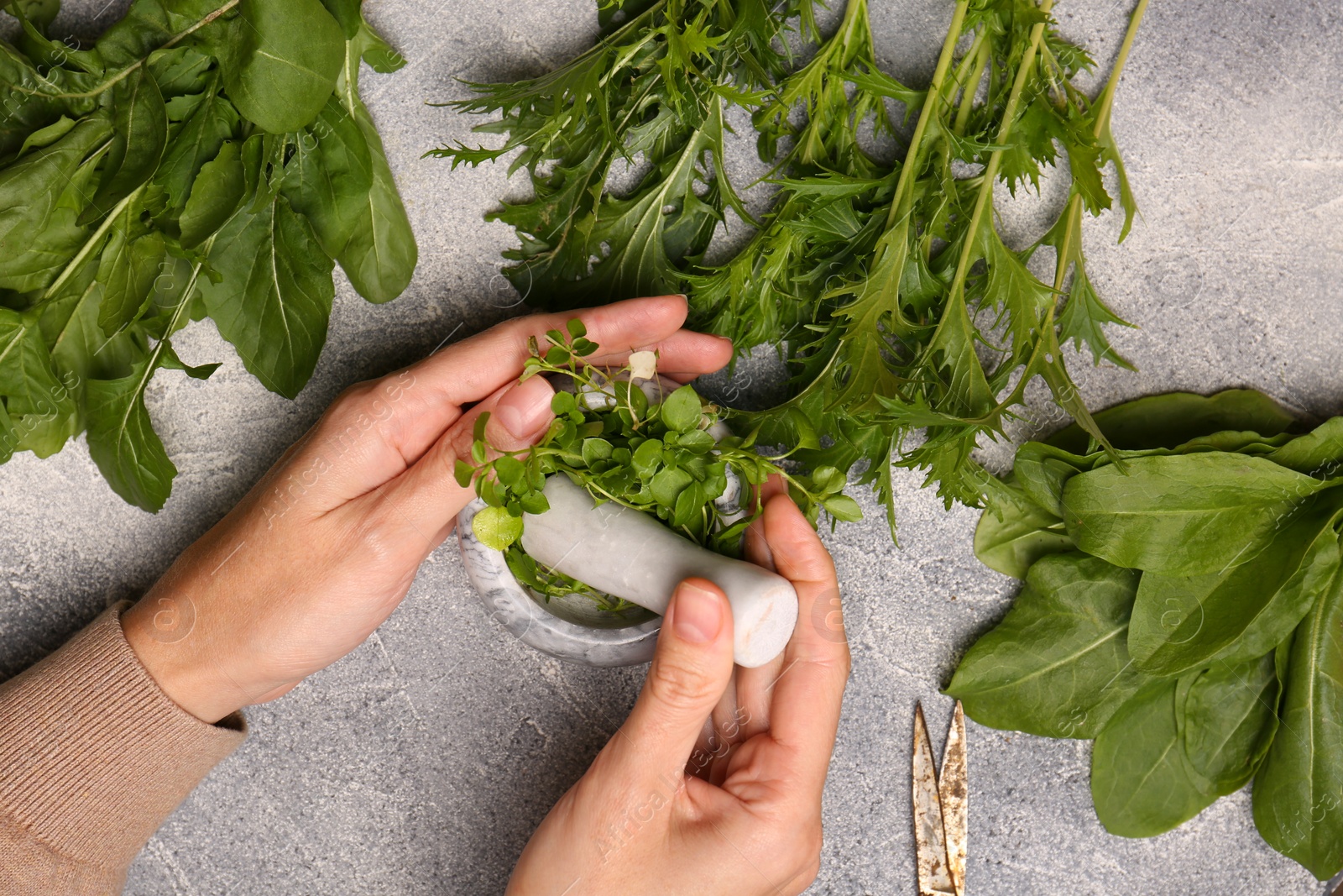 Photo of Woman grinding fresh green herbs in mortar at light grey table, top view