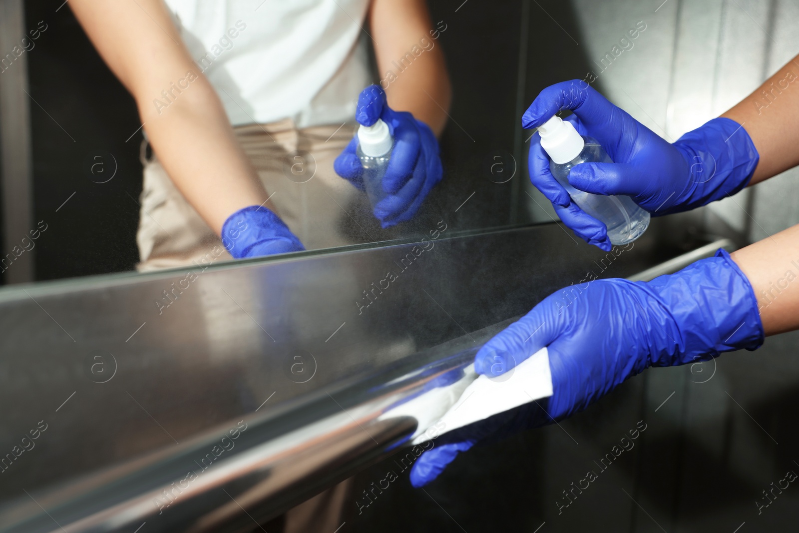 Photo of Woman wiping elevator`s handrails with detergent and paper napkin, closeup