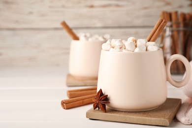 Cup of hot drink with marshmallows and aromatic cinnamon on white table. Space for text