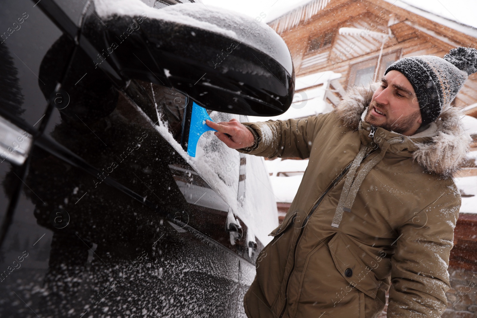 Photo of Young man cleaning snow from car window outdoors on winter day