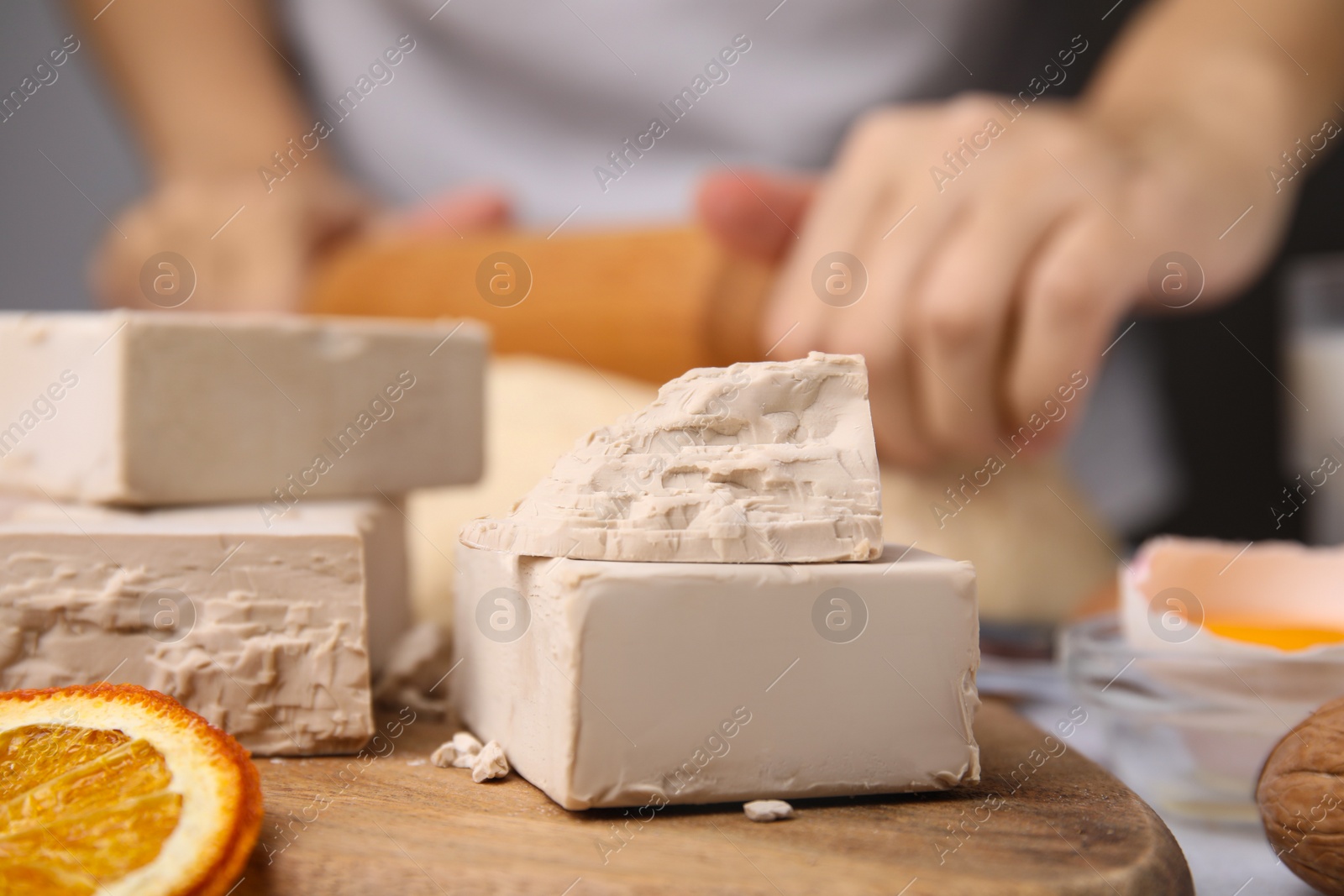 Photo of Woman kneading dough at table, focus on blocks of compressed yeast