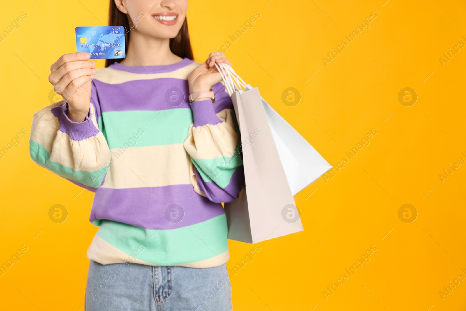 Photo of Woman with shopping bags and credit card on yellow background, closeup