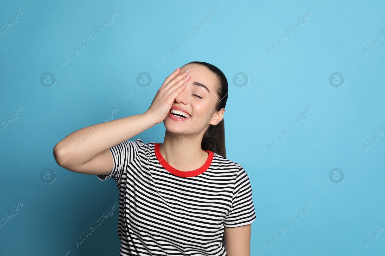 Photo of Beautiful young woman laughing on light blue background. Funny joke