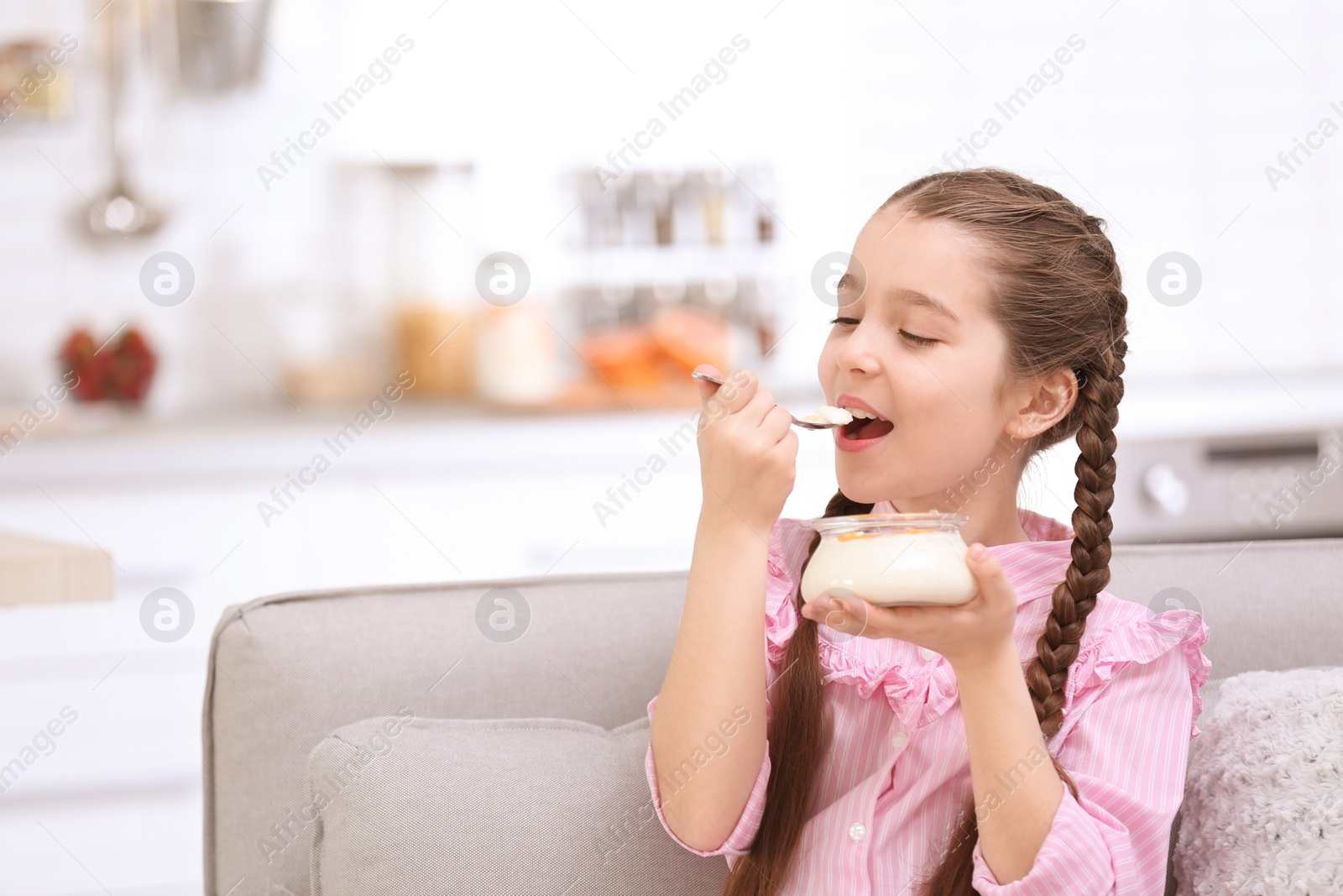 Photo of Cute girl eating tasty yogurt at home