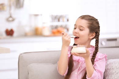 Cute girl eating tasty yogurt at home