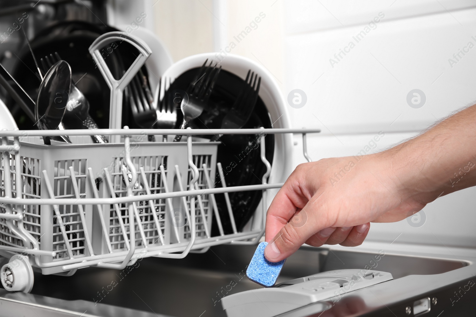 Photo of Woman putting detergent tablet into open dishwasher in kitchen, closeup