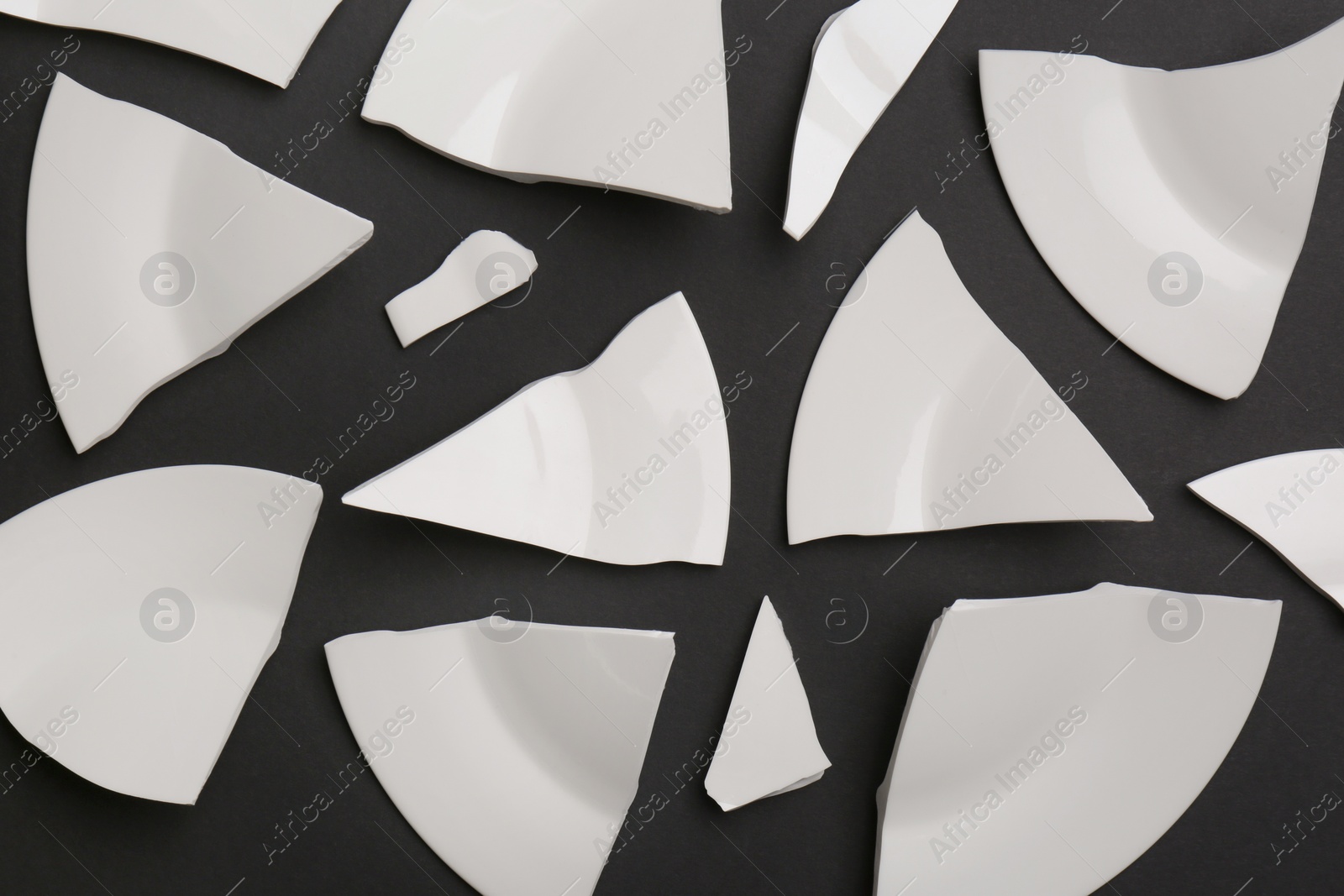 Photo of Pieces of broken white ceramic plate on dark grey background, flat lay