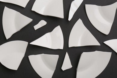 Photo of Pieces of broken white ceramic plate on dark grey background, flat lay