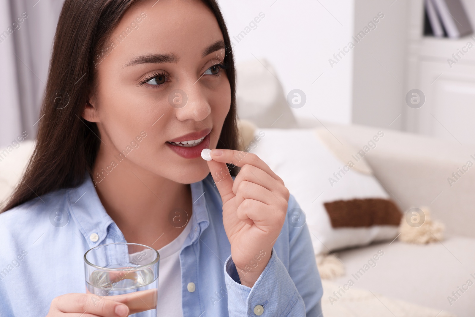 Photo of Beautiful woman with glass of water taking pill at home, space for text