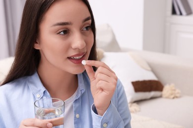 Photo of Beautiful woman with glass of water taking pill at home, space for text