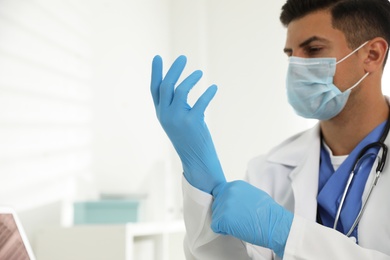 Photo of Doctor in protective mask putting on medical gloves in office