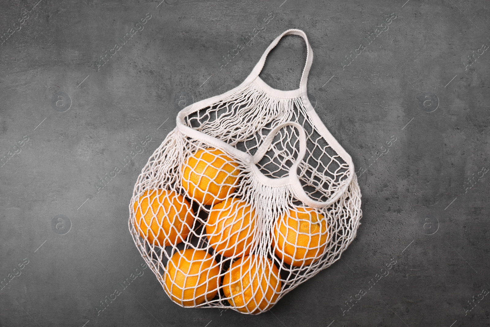 Photo of White net bag with oranges on grey table, top view