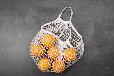 White net bag with oranges on grey table, top view