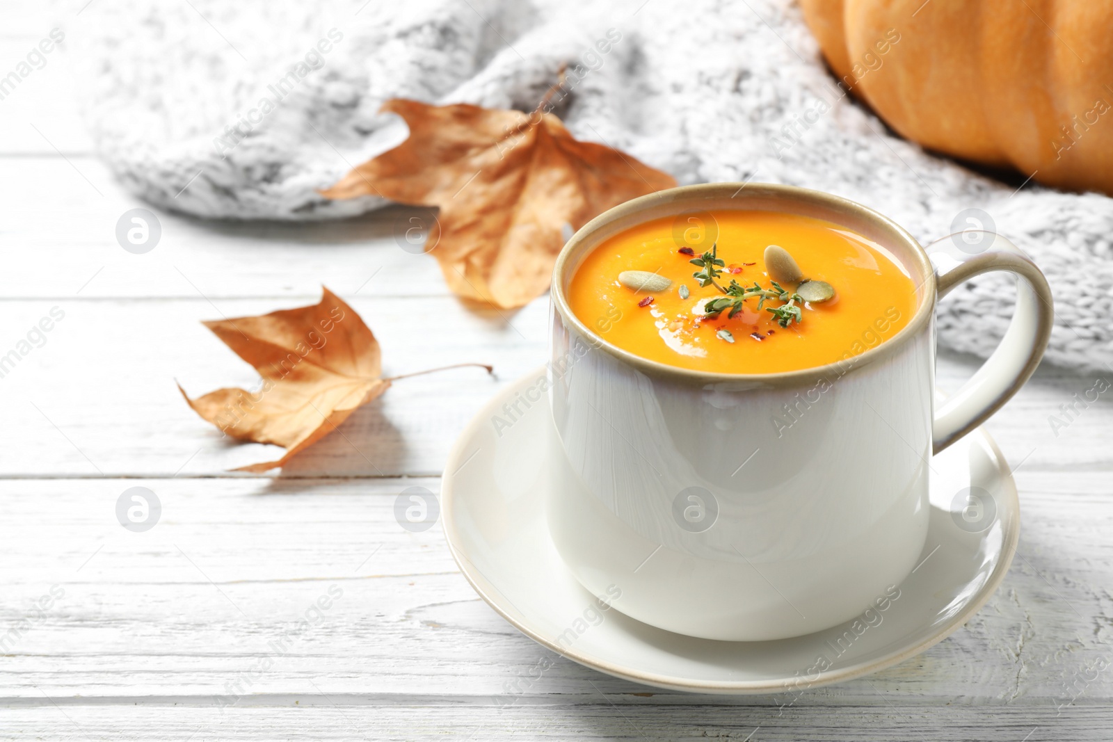 Photo of Delicious pumpkin soup in cup on white wooden table