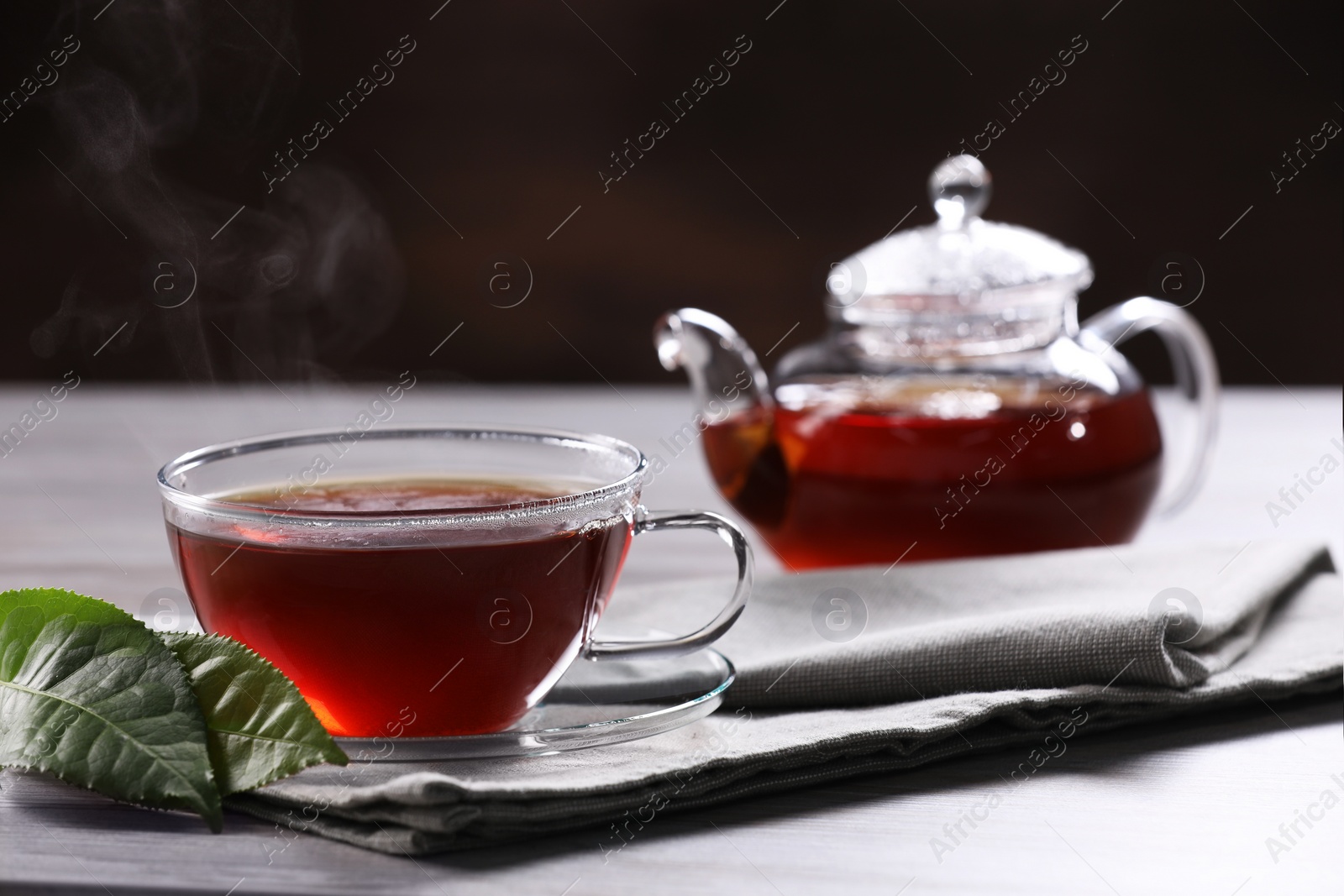 Photo of Aromatic hot tea in glass cup, teapot and leaves on light table. Space for text