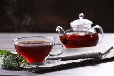 Aromatic hot tea in glass cup, teapot and leaves on light table. Space for text