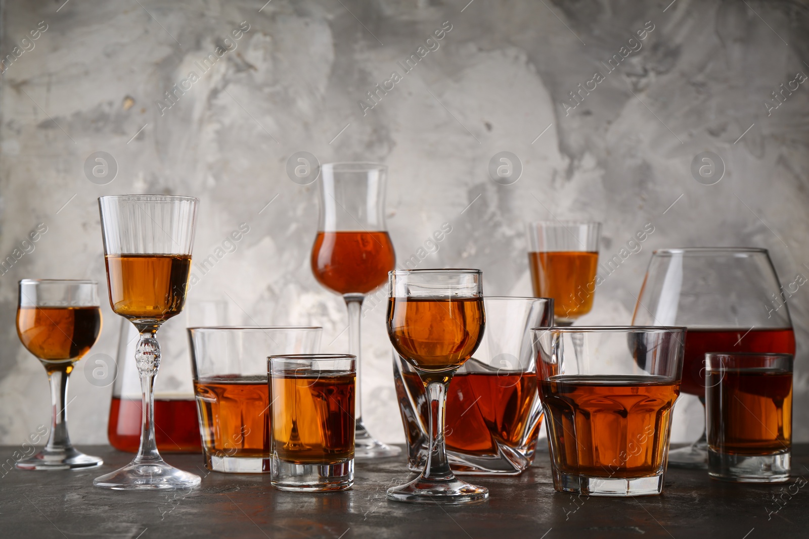 Photo of Different delicious liqueurs in glasses on grey table