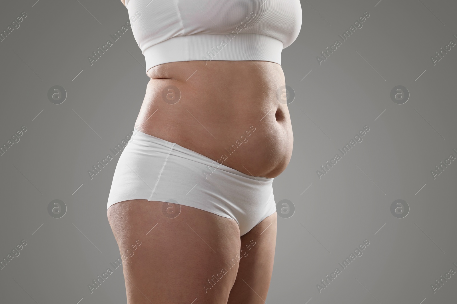 Photo of Woman with excessive belly fat on grey background, closeup. Overweight problem