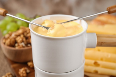 Photo of Pot of tasty cheese fondue and forks with bread pieces on wooden table