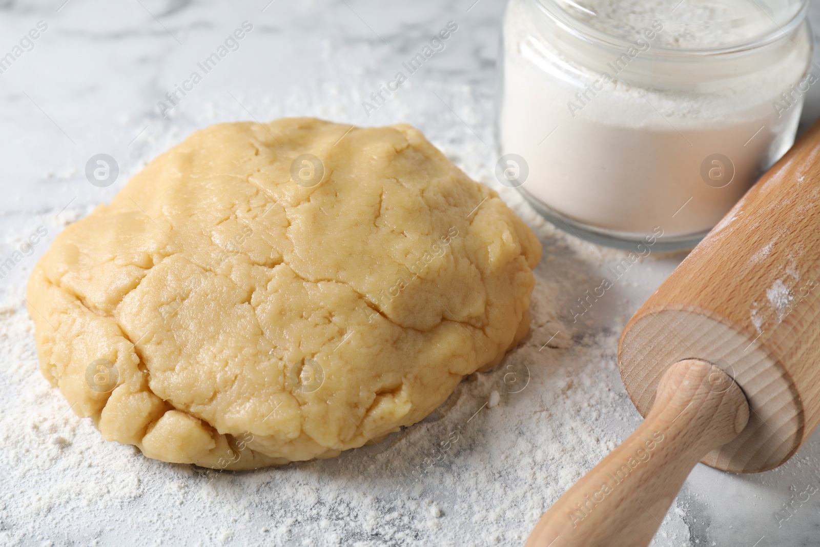 Photo of Making shortcrust pastry. Raw dough, flour and rolling pin on white marble table