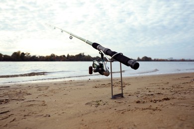 Fishing rod with reel on sand near river