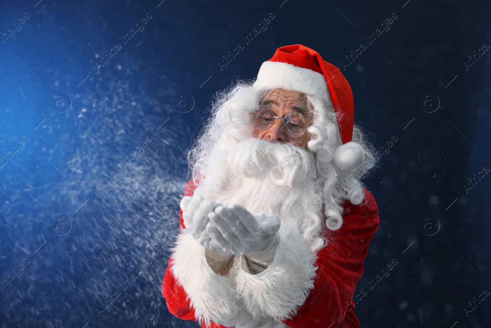 Photo of Merry Christmas. Santa Claus blowing snow on dark blue background