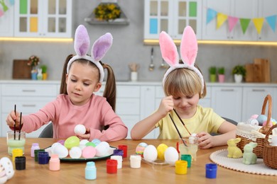 Children painting Easter eggs at table in kitchen