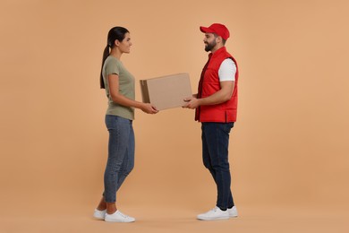 Photo of Smiling courier giving parcel to receiver on light brown background