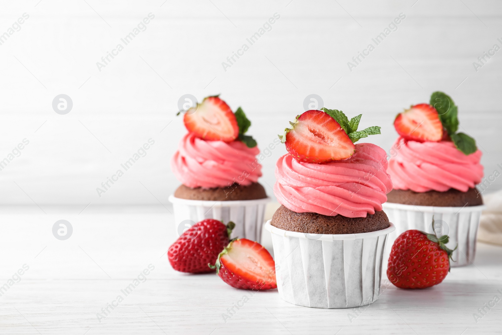 Photo of Sweet cupcakes with fresh strawberries on white table. Space for text