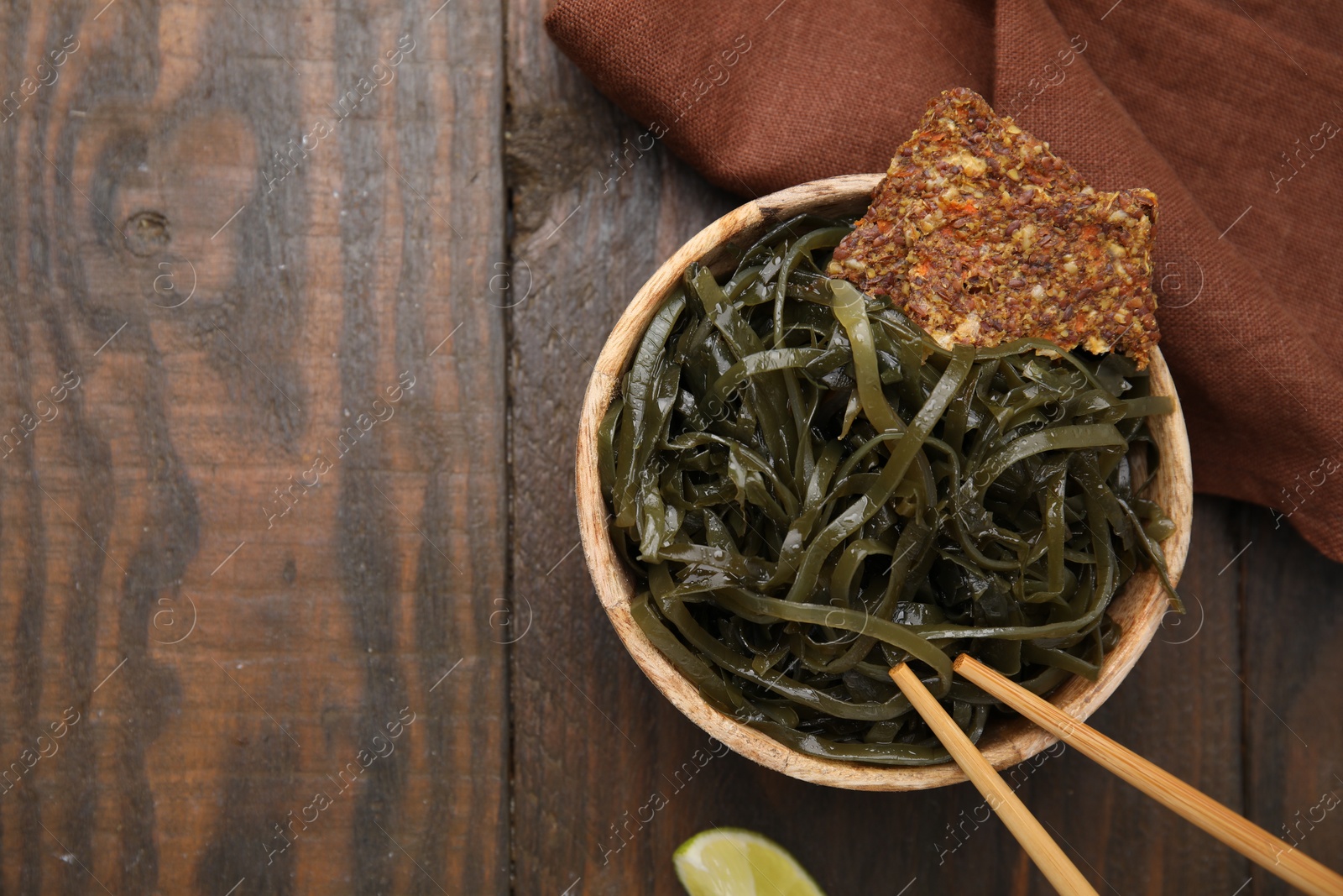 Photo of Tasty seaweed salad in bowl served on wooden table, flat lay. Space for text